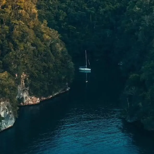 Sailboat in a narrow channel between forested cliffs in Los Haitises
